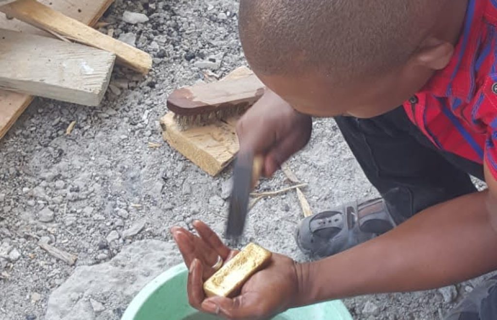 A man kneels, adding material to a bowl during the gold washing process at the New Liberian Mining Company site.