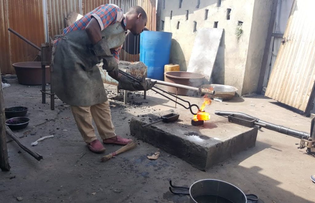 A man hammers a hot gold particle at the new Liberian mining company site, showcasing gold working techniques.