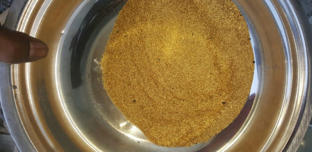 A hand holds a bowl of gold dust, symbolizing gold discovered at a new mining site in Liberia.