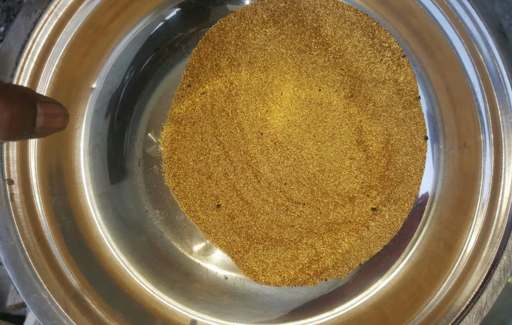 A hand holds a bowl of gold dust, symbolizing gold discovered at a new mining site in Liberia.